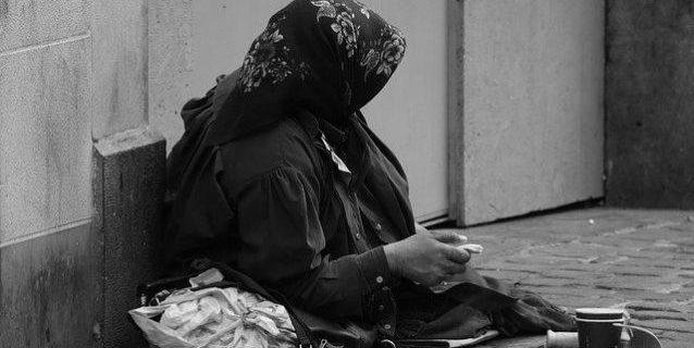 Bettlerin mit Kopftuch sitzt auf der Straße