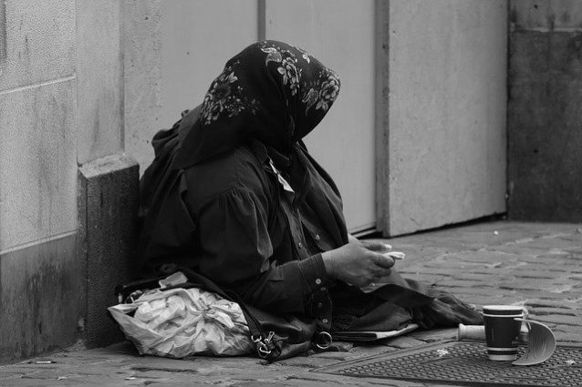 Bettlerin mit Kopftuch sitzt auf der Straße