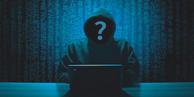 eine dunkle Gestalt mit Kapuze und Fragezeichen im Gesicht sitzt vor einem Laptop