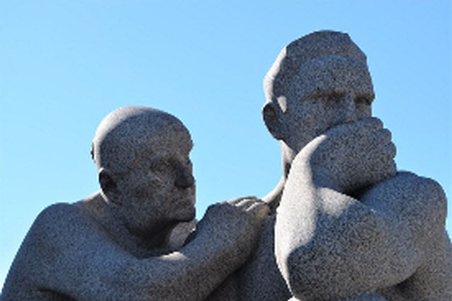 Zwei Männer aus Stein. Der eine legt dem anderen die Hand auf die Schulter. Der andere hält die Hand vor den Mund