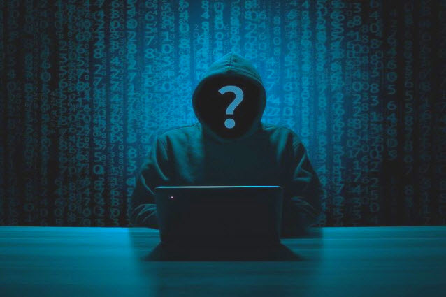 eine dunkle Gestalt mit Kapuze und Fragezeichen im Gesicht sitzt vor einem Laptop