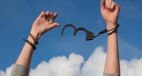 Zwei Hände mit Handschellen. An der einen Hand ist die Handschelle geschlossen. Die andere wurde davon befreit.